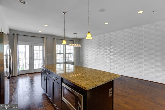 kitchen with a center island, pendant lighting, dark wood finished floors, stainless steel appliances, and light stone countertops