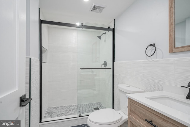 full bathroom with tile walls, visible vents, toilet, a shower stall, and vanity