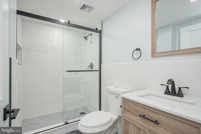 bathroom featuring a stall shower, visible vents, toilet, vanity, and tile walls