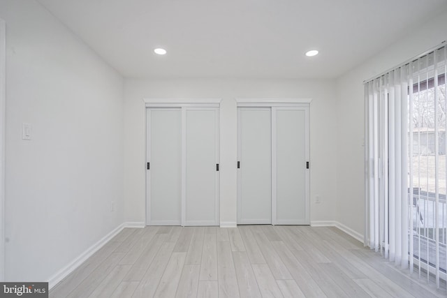 unfurnished bedroom featuring baseboards, two closets, light wood-style flooring, and recessed lighting