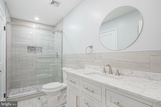 full bath featuring visible vents, toilet, vanity, a shower stall, and tile walls