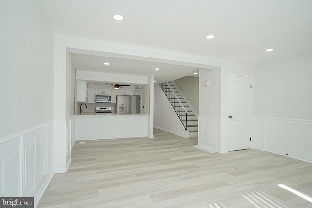 empty room with light wood finished floors, stairway, a sink, and recessed lighting