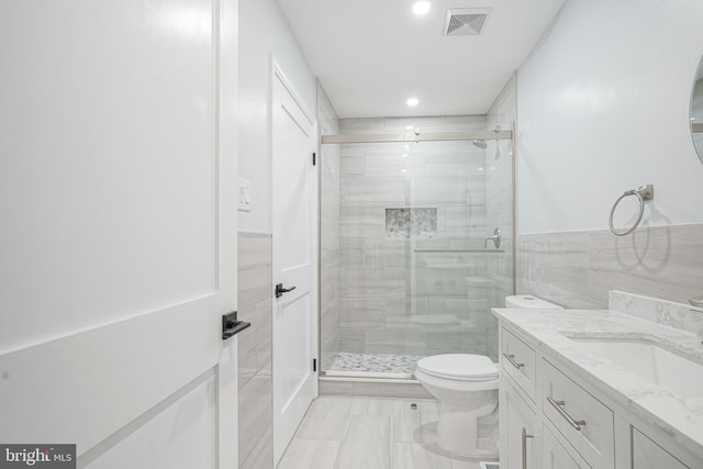 bathroom with visible vents, toilet, vanity, a shower stall, and tile walls