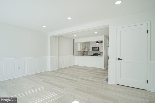 unfurnished room featuring a decorative wall, recessed lighting, a sink, wainscoting, and light wood finished floors