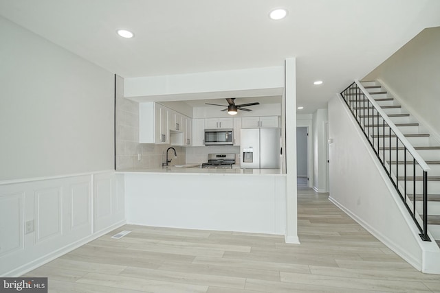 kitchen with stainless steel appliances, light countertops, white cabinetry, a sink, and a peninsula