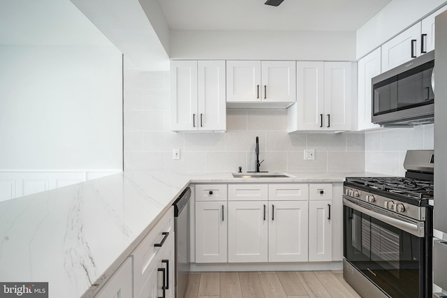 kitchen with tasteful backsplash, appliances with stainless steel finishes, light stone countertops, white cabinetry, and a sink