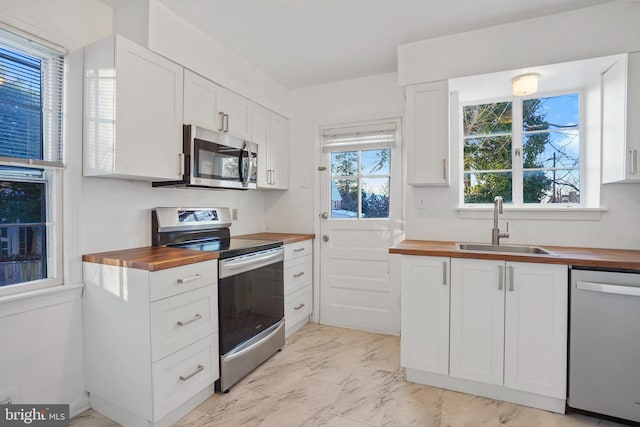 kitchen with butcher block counters, marble finish floor, stainless steel appliances, white cabinetry, and a sink