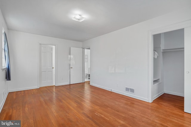 unfurnished bedroom with light wood finished floors, baseboards, a spacious closet, and visible vents