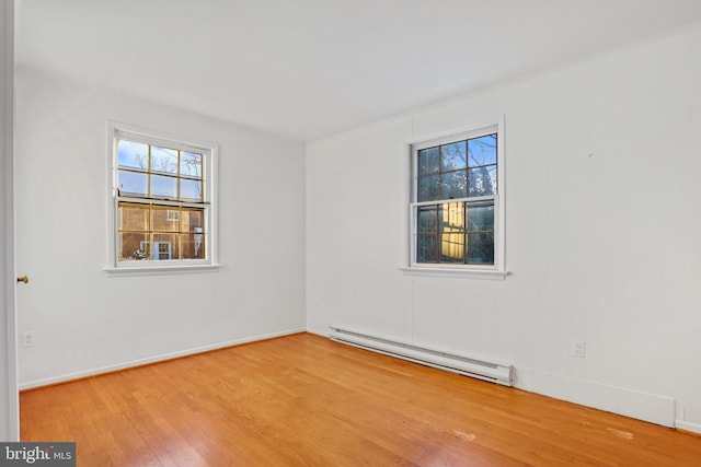 empty room featuring a baseboard heating unit, light wood finished floors, and baseboards