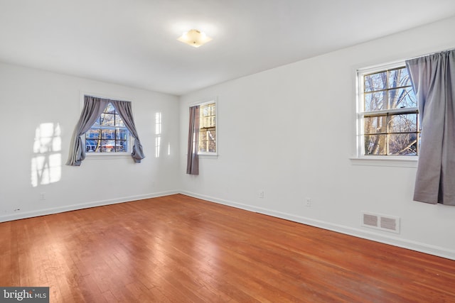 unfurnished room with visible vents, plenty of natural light, baseboards, and wood finished floors