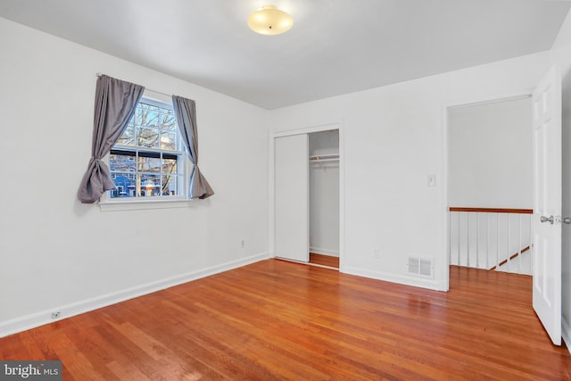 unfurnished bedroom featuring a closet, wood finished floors, visible vents, and baseboards