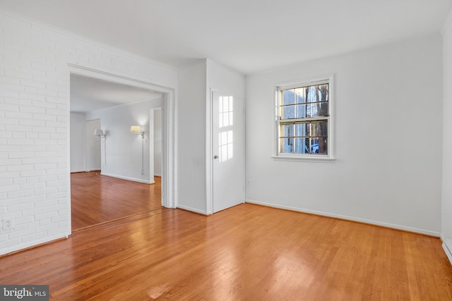 spare room featuring brick wall, baseboards, and wood finished floors