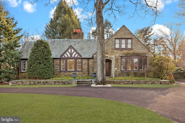 tudor house featuring stone siding, a front lawn, and a chimney