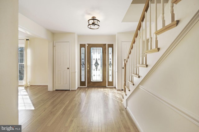 foyer entrance featuring light wood finished floors, baseboards, and stairway