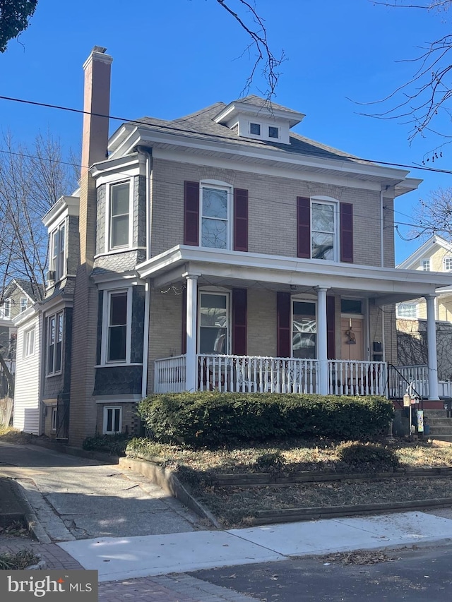 american foursquare style home featuring covered porch, brick siding, and a chimney