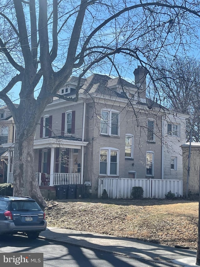 view of front of house with covered porch, a chimney, and fence