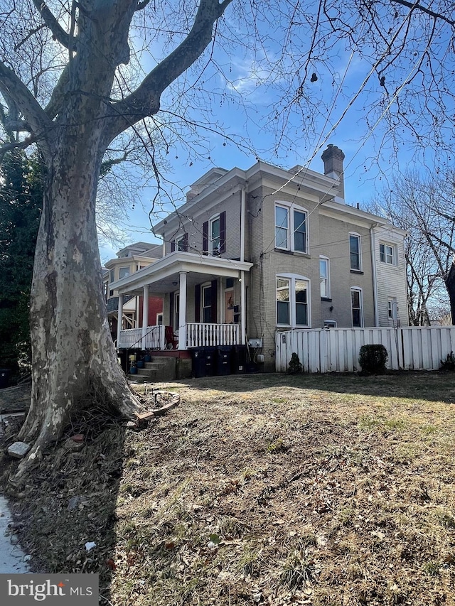 view of side of home featuring covered porch, a chimney, fence, and brick siding