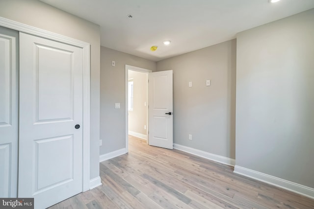 unfurnished bedroom featuring light wood finished floors, baseboards, and a closet