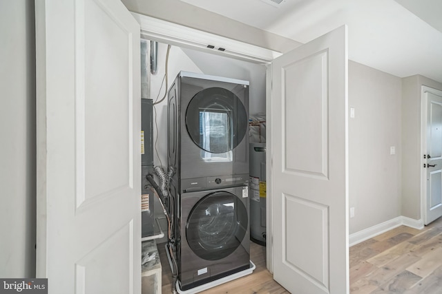 clothes washing area featuring laundry area, stacked washer / dryer, baseboards, water heater, and light wood finished floors