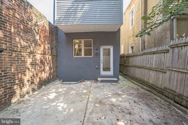 view of exterior entry with a patio area, fence, and stucco siding