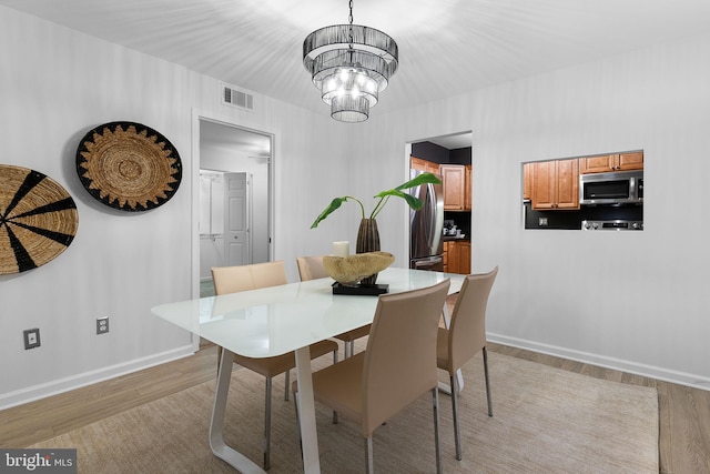 dining area featuring light wood-type flooring, visible vents, a notable chandelier, and baseboards