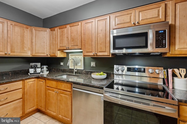 kitchen with light tile patterned floors, stainless steel appliances, dark stone countertops, and a sink