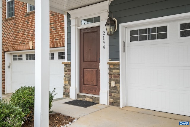 entrance to property featuring a garage, stone siding, and brick siding