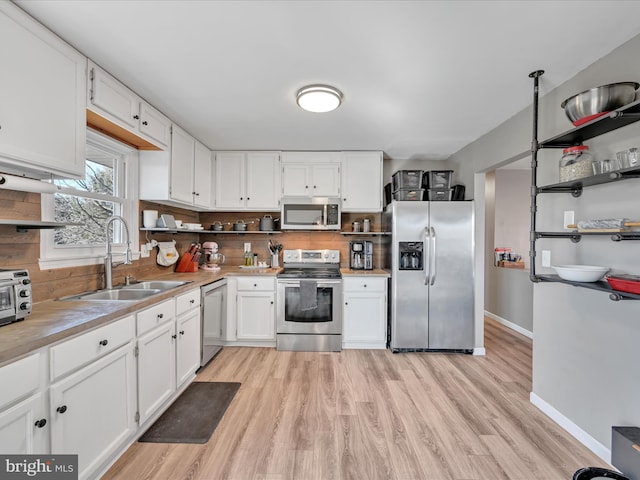 kitchen featuring light countertops, light wood-style flooring, white cabinets, stainless steel appliances, and a sink