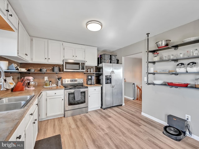 kitchen with open shelves, light wood-style flooring, a sink, stainless steel appliances, and white cabinets