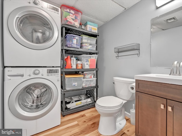 bathroom with wood finished floors, visible vents, stacked washing maching and dryer, a drop ceiling, and toilet