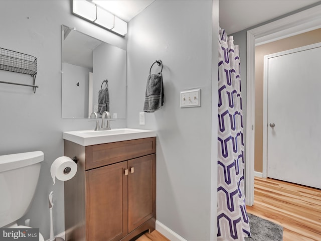 bathroom featuring baseboards, toilet, wood finished floors, and vanity