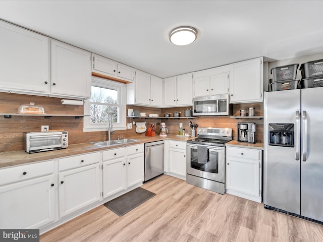 kitchen with a sink, light wood-type flooring, appliances with stainless steel finishes, and white cabinets