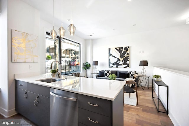 kitchen featuring pendant lighting, light countertops, a sink, dark cabinets, and dishwasher