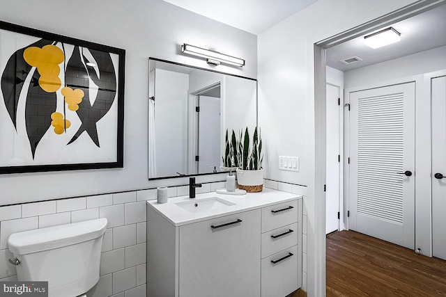 bathroom with tile walls, visible vents, toilet, vanity, and wood finished floors