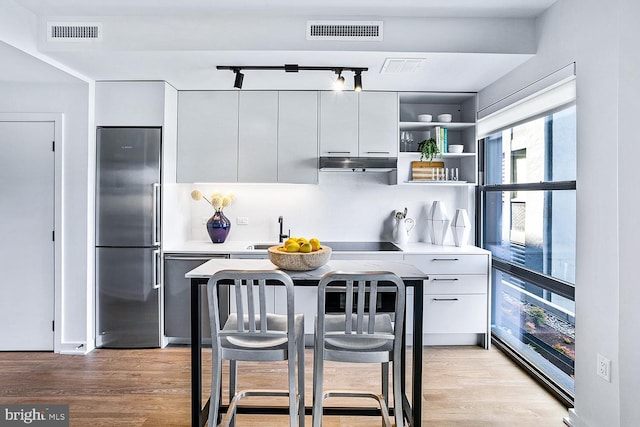 kitchen featuring light countertops, visible vents, white cabinets, under cabinet range hood, and built in refrigerator