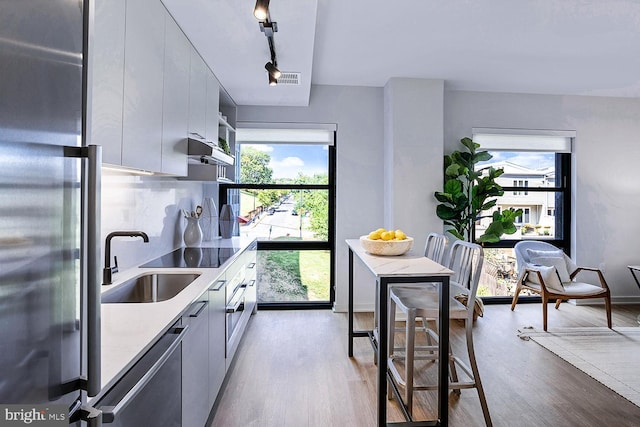 kitchen with stainless steel appliances, wood finished floors, a sink, and white cabinets