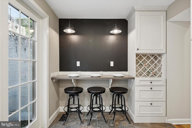 kitchen with baseboards, decorative light fixtures, a kitchen bar, white cabinetry, and backsplash