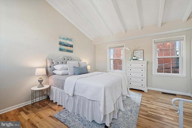 bedroom featuring lofted ceiling with beams, visible vents, baseboards, and wood finished floors