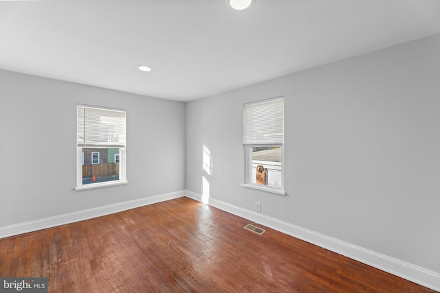 spare room with plenty of natural light, wood finished floors, visible vents, and baseboards