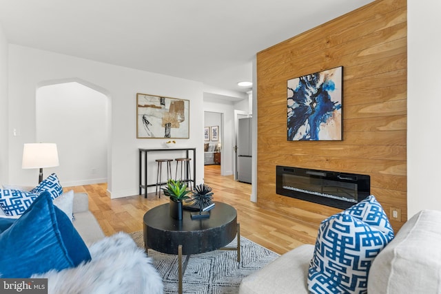 living room with arched walkways, recessed lighting, a glass covered fireplace, wood finished floors, and baseboards