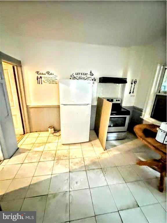 kitchen featuring light tile patterned floors, electric range, freestanding refrigerator, and range hood