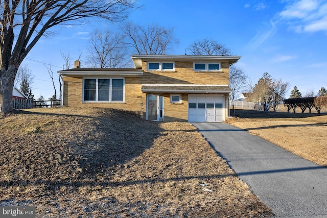 split level home featuring brick siding, a chimney, an attached garage, fence, and driveway