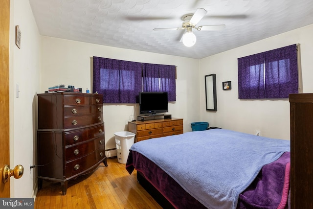 bedroom with a ceiling fan, baseboard heating, and wood finished floors