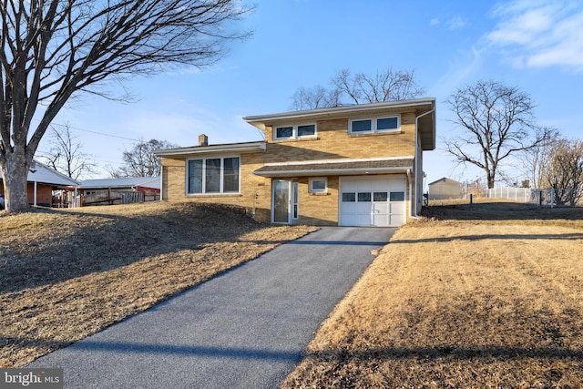 tri-level home featuring a garage, aphalt driveway, a chimney, and brick siding