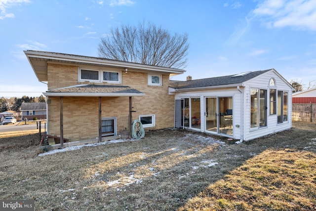 rear view of house featuring a yard, brick siding, and fence