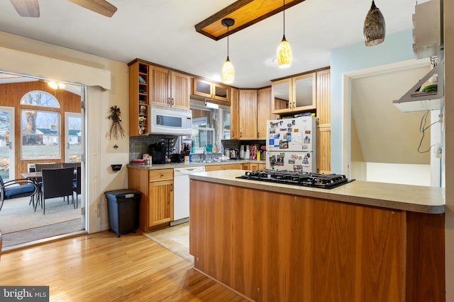 kitchen with a peninsula, white appliances, light countertops, light wood finished floors, and pendant lighting