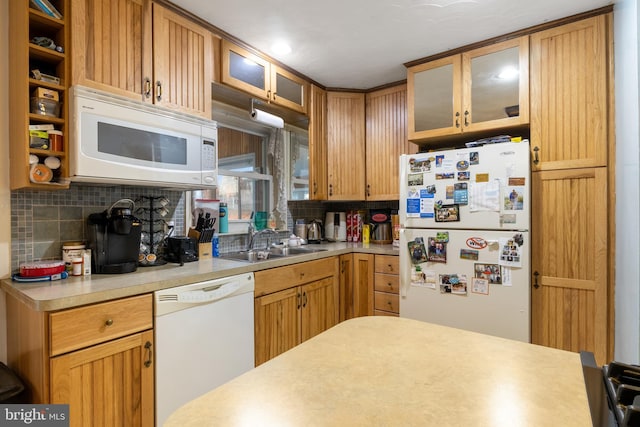 kitchen featuring light countertops, backsplash, glass insert cabinets, a sink, and white appliances