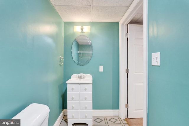 half bath with a drop ceiling, toilet, vanity, and baseboards