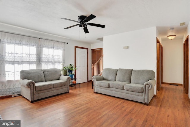 living room featuring a ceiling fan, stairs, baseboards, and wood finished floors