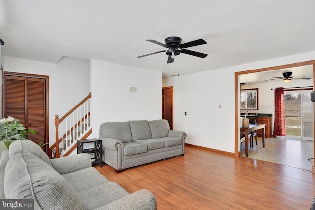 living area with baseboards, stairway, a ceiling fan, and light wood-style floors